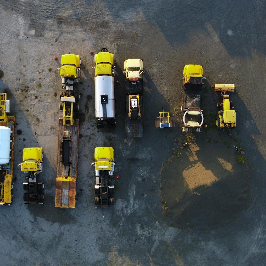 Overhead view of yellow construction trucks parked in neat rows on a gravel surface.